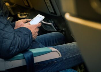 Man hand holding smartphone on board for chat and planning the trip. Male traveler using smartphone surfing the internet and chat during flight.