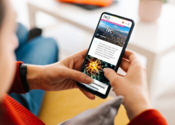 Unrecognizable young woman holding a mobile phone with white screen at home - Mockup for advertisement